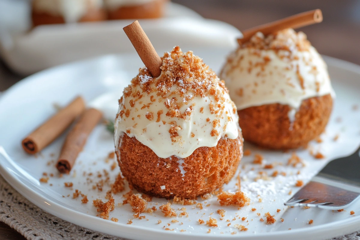 A close-up of two carrot cake bombs topped with cream cheese frosting, crumbled brown sugar, and a cinnamon stick, showcasing the irresistible appeal of this dessert trend.