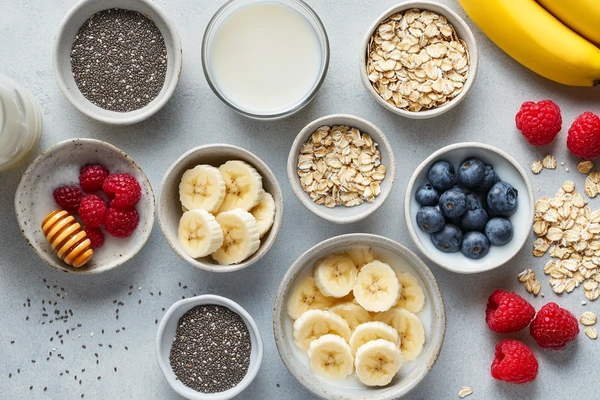 Top-down view of chia seeds, flax seeds, oats, bananas, raspberries, and blueberries arranged for oatmeal preparation.