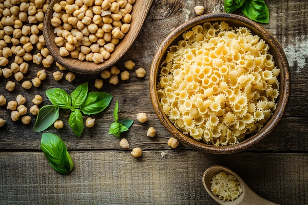 Chickpea pasta and raw chickpeas with basil leaves, showcasing the ingredients behind chickpea pasta taste like pasta.