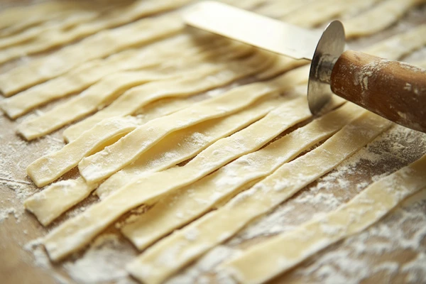 Freshly rolled and cut dough strips on a floured surface with a cutter, ready to make seasoned Fritos.