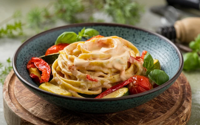 Pasta coated in Garlic-Parmesan sauce, garnished with roasted vegetables and basil.