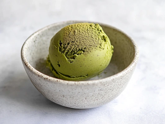 A single scoop of matcha ice cream in a textured ceramic bowl.